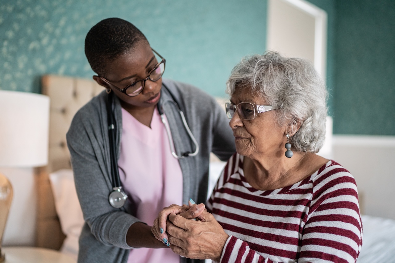 Home caregiver helping a senior adult woman standing in the bedroom.