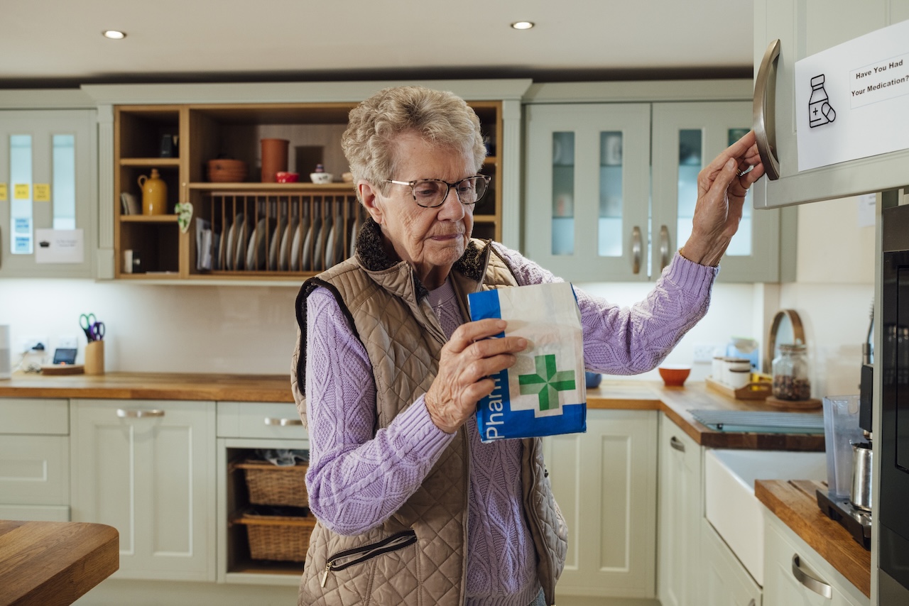 Senior adult woman is in the kitchen where she is putting prescription medication into a cupboard.