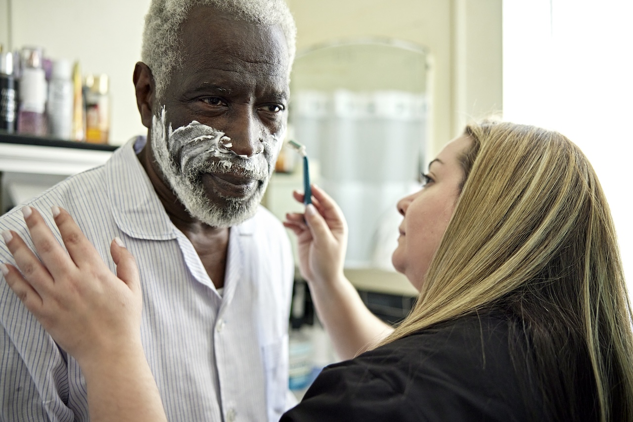 Woman shaving beard of senior adult man